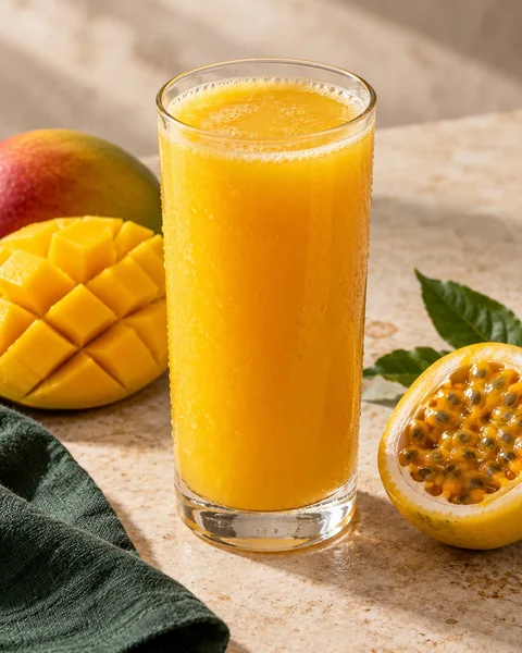Suco dourado de manga com maracujá, ao lado das frutas.